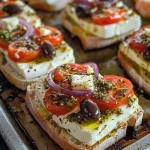 ['Close-up view of Mediterranean Baked Feta Bruschetta topped with pesto shrimp.', 'Juicy bruschetta with baked feta, shrimp, tomatoes, and olives on a rustic plate.', 'A side view of toasted bread topped with feta cheese and vibrant Mediterranean ingredients.', 'Overhead shot of bruschetta with colorful toppings including shrimp and cherry tomatoes.']