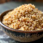 ['Close-up of a textured pile of quinoa flour in a wooden bowl.', 'Side view of light-colored quinoa flour on a dark surface.', 'Quinoa flour showcased in a well-lit kitchen setting.', 'A small heap of quinoa flour with whole quinoa seeds beside it.']