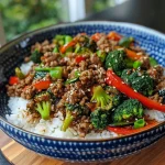 ['A close-up view of a spicy ground beef stir-fry bowl with colorful vegetables and rice.', 'Side perspective of a vibrant stir-fry bowl featuring ground beef, broccoli, and bell peppers, served over rice.', 'Juicy spicy ground beef stir-fry topped with garlic veggies, presented in a bowl with steamed rice.', 'A detailed shot of a stir-fry bowl showcasing ground beef, zucchini, and mushrooms against a backdrop of white rice.']