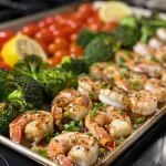['Close-up of a sheet pan filled with spicy garlic shrimp and vibrant vegetables.', 'Juicy shrimp and colorful broccoli and tomatoes arranged on a sheet pan.', 'A side view of delicious shrimp with garlic and vegetables on a baking tray.', 'Freshly cooked spicy shrimp and vegetables presented on a sheet pan.']