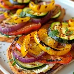 ['Close-up shot of grilled vegetable toast featuring zucchini, bell peppers, and red onion.', 'Side view of a plated grilled vegetable toast topped with goat cheese and mint leaves.', 'Juicy grilled vegetable toast with colorful toppings, including yellow and red vegetables.', 'A vibrant serving of grilled vegetable toast showcasing fresh ingredients and creamy cheeses.']