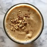 Close-up of a creamy apple smoothie in a glass with a straw, garnished with apple slices.