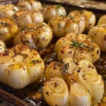 Close-up view of golden-brown baked garlic heads with a shiny olive oil glaze.