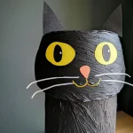 A close-up of a black cat craft made from a paper roll, showcasing its painted features and details.