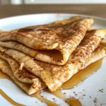 Close-up of cinnamon roll protein crepes drizzled with honey and garnished with cream cheese.