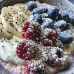 Close-up side view of a vibrant bowl of berry cheesecake overnight oats, showcasing blueberries and creamy texture.