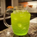 A vibrant green drink in a clear glass with ice cubes, garnished with a slice of pineapple.