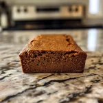 A side view of a golden-brown gingerbread loaf with a textured surface.