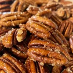 Close-up of shiny, golden-brown maple candied pecans on a wooden surface.